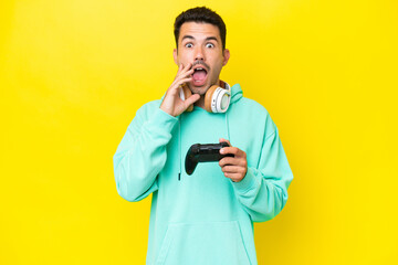 Young handsome man playing with a video game controller over isolated wall with surprise and...