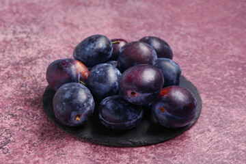 Black board with fresh plums on purple background