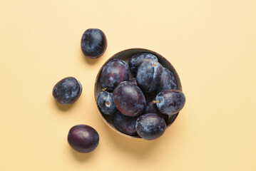 Bowl with fresh plums on yellow background