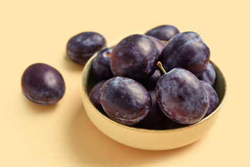 Bowl with fresh plums on yellow background