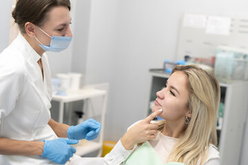 a female dentist talking to patient sad girl complaining of tereble toothache, holding her jaw in the clinic