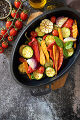 Grilled vegetables: red and yellow paprika, garlic, zucchini, eggplants, carrots in a frying pan on a dark stone background. View from above. Copy space.