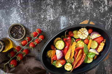 Grilled vegetables: red and yellow paprika, garlic, zucchini, eggplants, carrots in a frying pan on a dark stone background. View from above. Copy space.