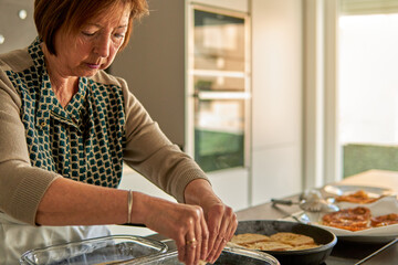 Abuela remojando pan en leche y huevo mientras frie las torrijas en una sartén en la encimera de...
