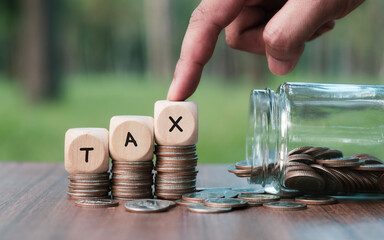 The word Tax in a wooden block placed on a coin with a human hand holding a wooden block. The...