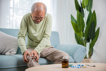 Old age. Asian senior man retirement knee joint pain on sofa, Elderly old man sitting down hands...