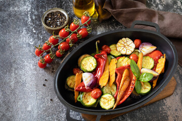 Grilled vegetables: red and yellow paprika, garlic, zucchini, eggplants, carrots in a frying pan on a dark stone background. Copy space.