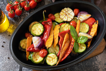 Grilled vegetables: red and yellow paprika, garlic, zucchini, eggplants, carrots in a frying pan on a dark stone background.