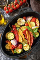 Grilled vegetables: red and yellow paprika, garlic, zucchini, eggplants, carrots in a frying pan on a dark stone background.