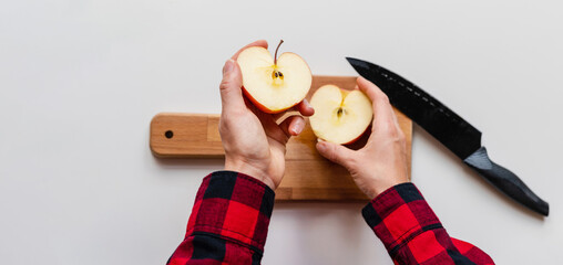 Two halves of an apple in male hands high angle view. Man cuts apple using knife.
