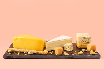 Board with tasty cheese, nuts and grissini on pink background