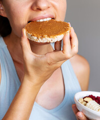 Female person eating healthy crispbread with peanut butter close-up.