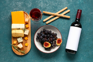 Tasty cheese, grissini, fruits, bottle and glass of wine on green background