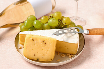 Plate with tasty cheese and grapes on white background
