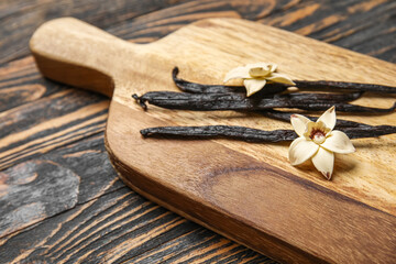 Board with aromatic vanilla sticks and flowers on black wooden background