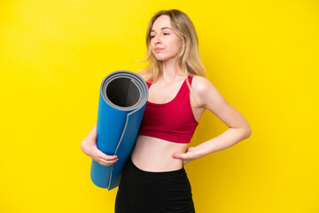 Young sport caucasian woman going to yoga classes while holding a mat isolated on yellow background suffering from backache for having made an effort