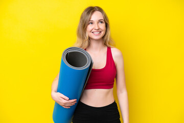 Young sport caucasian woman going to yoga classes while holding a mat isolated on yellow background thinking an idea while looking up