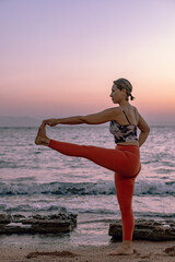Young beautiful lady practice yoga on the beach at sunrise