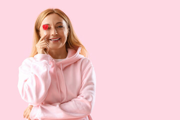 Mature woman in hoodie with lollipop on pink background