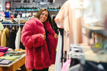 Young woman in fur coat choosing winter clothes in a clothing store.