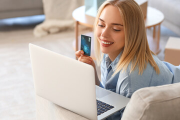 Beautiful young woman with laptop and credit card shopping online at home