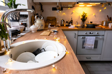 Dirty dishes in the sink in the garlanded kitchen, a holiday after a feast at Christmas. Mess after...