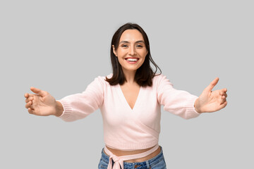 Young woman opening arms for hug on light background