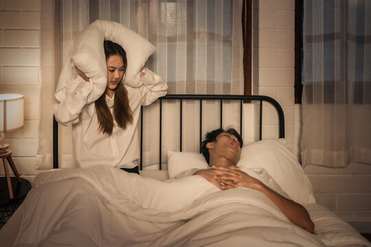 exasperated woman covers ears to muffle partner's loud snoring at night