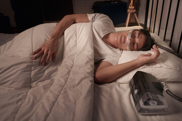 Asian man using CPAP mask and machine for sleep apnea treatment at home