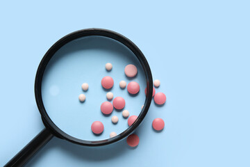 Magnifier with different pills on blue background
