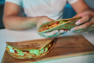 a young man, wearing latex gloves, preparing a falafel sandwich in a pita bread, with chopped...