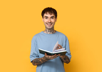 Young tattooed man with book on yellow background