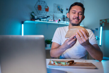 a young man, wearing latex gloves, preparing a falafel sandwich in a pita bread, with chopped...