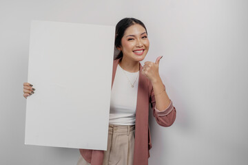 Smiling young Asian woman employee holding and showing empty blank board and gesturing thumbs up for approval, isolated by white background
