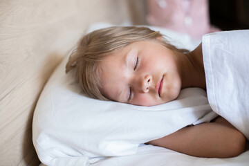 Obraz na płótnie Canvas A charming little girl with long hair is peacefully sleeping in a comfortable bed on a pristine white pillow at the morning. It's perfect for projects related to family, childhood, or relaxation.