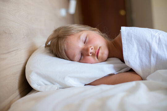 A little girl with long hair is peacefully sleeping in a comfortable bed on a white pillow at the morning. Close up shot.It's perfect for projects related to family, childhood, or relaxation.