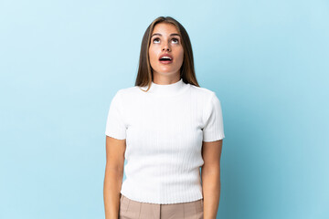 Young Uruguayan woman isolated on blue background looking up and with surprised expression