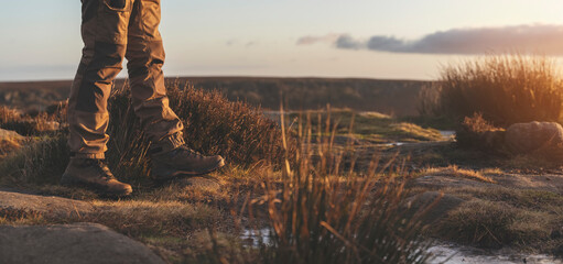 man in special boots walking in the mountains reaching the destination and on the top of mountain in Peak District at sunset on autumn day Travel Lifestyle concept - obrazy, fototapety, plakaty