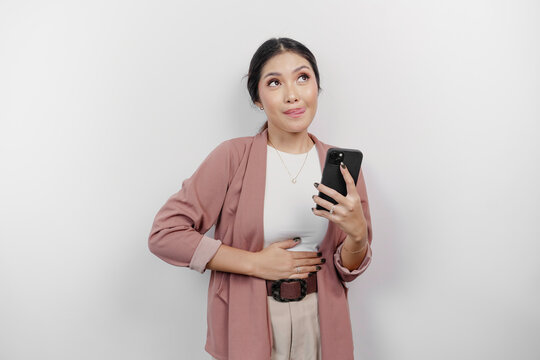 A hungry Asian woman employee is holding her phone and imagining yummy food she wants to order, isolated on white color background.