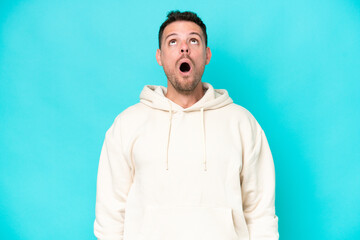 Young caucasian handsome man isolated on blue background looking up and with surprised expression