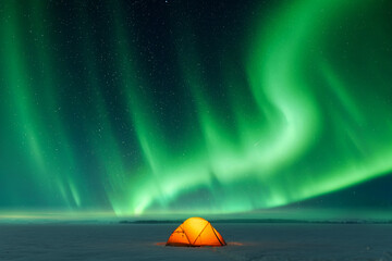 Orange tent lighted from the inside against the backdrop of incredible sky with Northern lights. Aurora borealis in winter field - obrazy, fototapety, plakaty