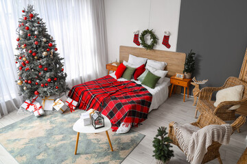 Interior of festive bedroom with cozy bed, Christmas tree, gift boxes and plaid blanket