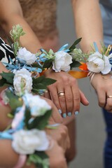 The bride and bridesmaids stand in a circle and hold hands with white flower bracelets, corsages....