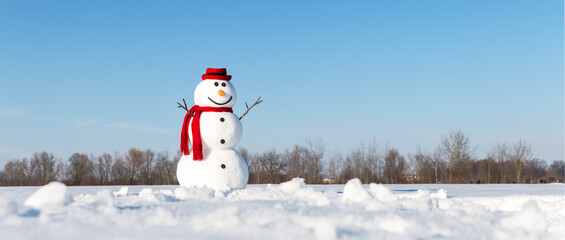 An amusing snowman, adorned with a trendy red hat and red scarf, graces a snow-covered field with a backdrop of brilliant blue skies. Christmas postcard