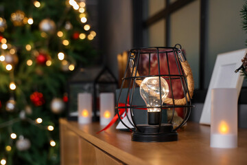 Fototapeta na wymiar Glowing lantern with Christmas decorations on wooden cabinet in festive living room, closeup