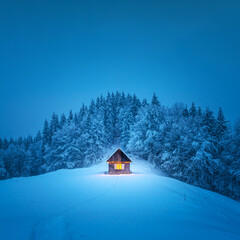 A winter scene with a solitary wooden cabin and snow-covered fir trees in the midst of a forested...