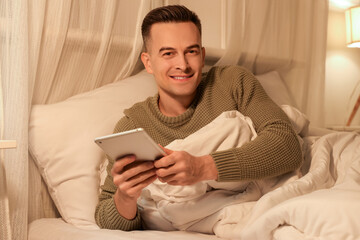 Handsome man using tablet computer in bedroom at night