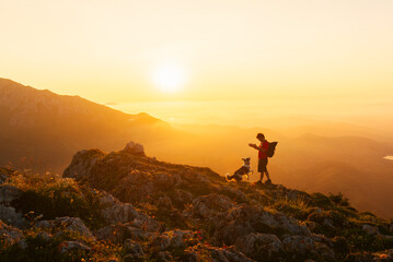 Mountaineer man with backpack plays with his border collie dog while hiking in the mountains at...