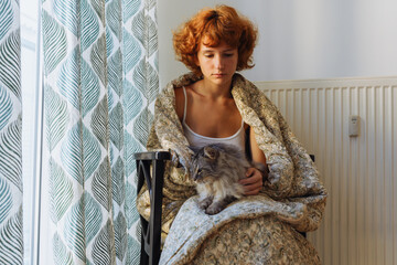 Girl hugging cat, sitting in blanket at home, frozen