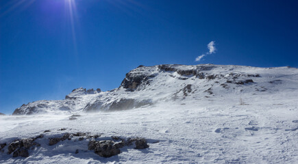 Winter landscape of the Italian mountains. View of the mountains near the Cinque Torri. Ray of light. Wind that raises the snow creating a mist. Particular light, blue intensity.